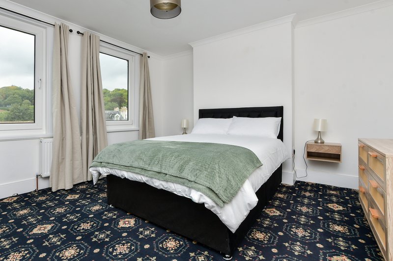 Bright bedroom with double bed, green quilt, black headboard, wooden nightstands and patterned carpet