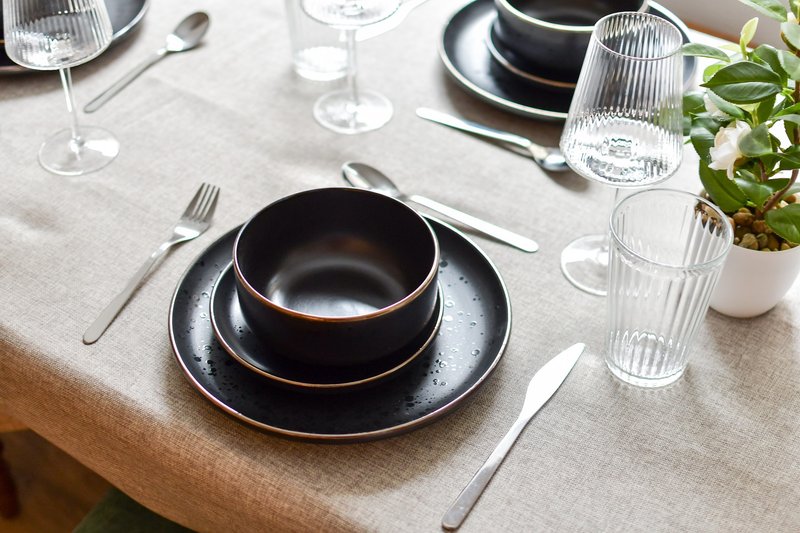 Dining table set with black plates, cutlery, glasses and potted plant