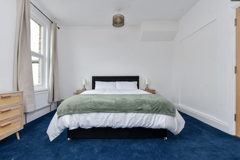 Bright bedroom with double bed, green bedding, blue carpet, wooden dresser and window