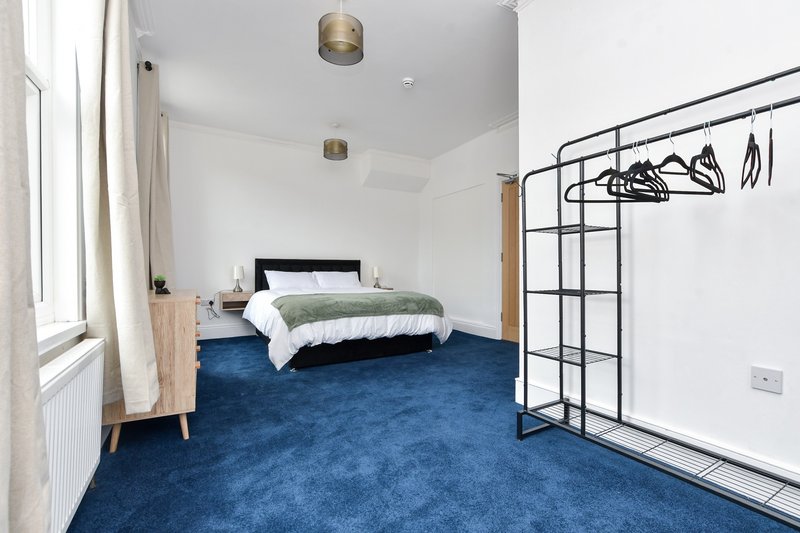 Bright bedroom with double bed, blue carpet, wooden nightstand and metal clothing rack