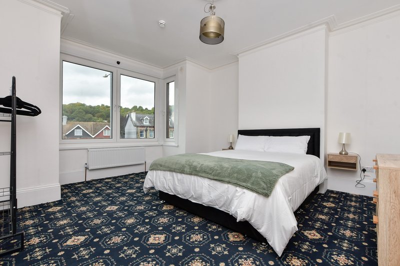 Bright bedroom with double bed, patterned blue carpet, window view and pendant light