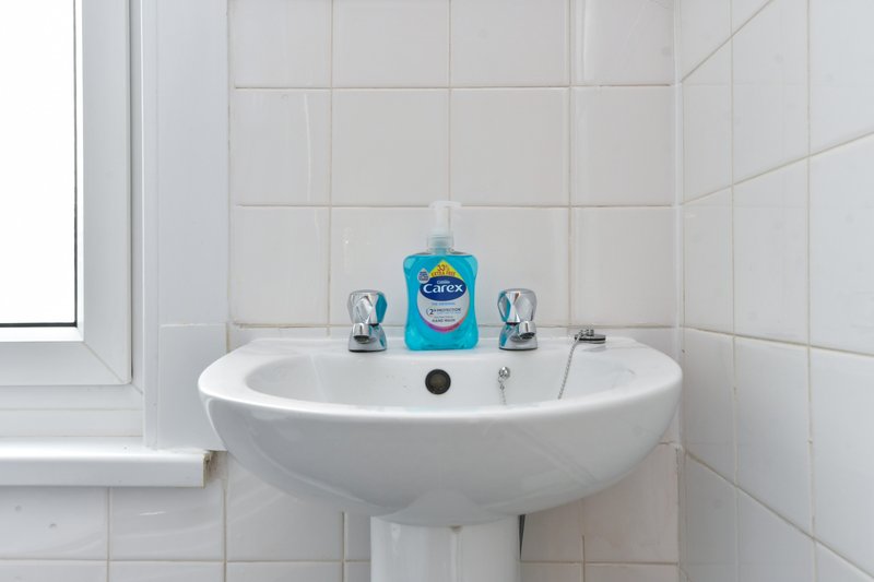 Clean white bathroom with round pedestal sink, chrome taps and soap dispenser