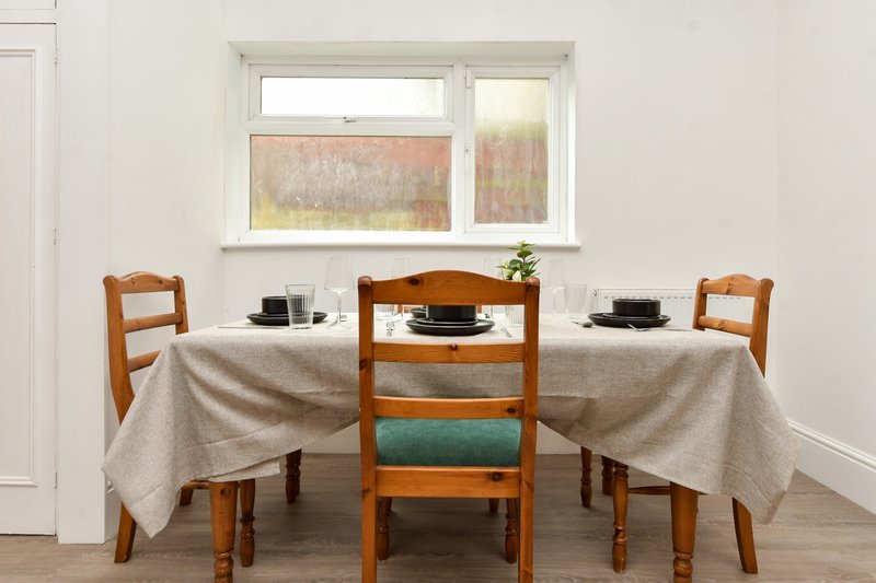 Dining room with round table, wooden chairs, beige tablecloth and window view