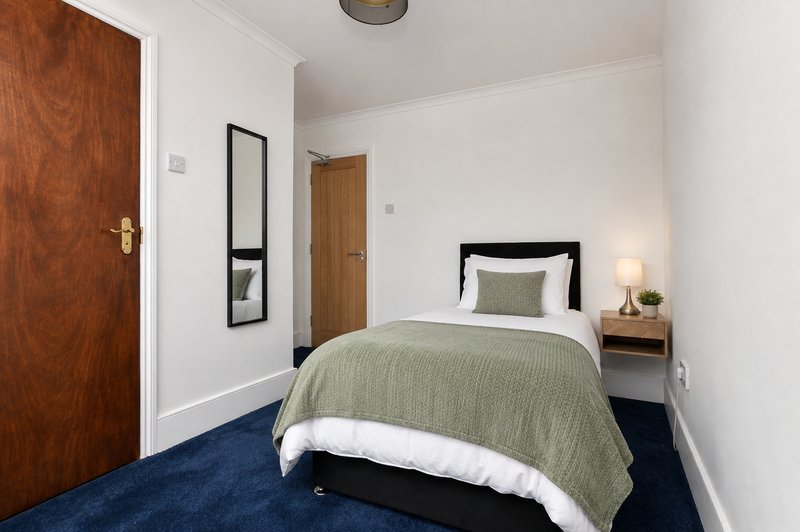 Compact bedroom with single bed, sage bedding, wooden doors, and blue carpet flooring