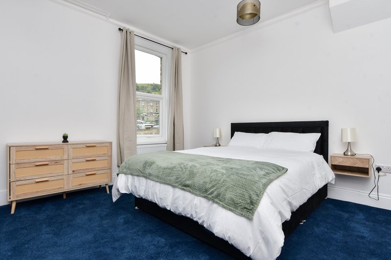 Bright bedroom with queen bed, wooden dresser, blue carpet and window with countryside view