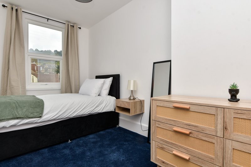 Bedroom with black bed, wooden dresser, blue carpet, and window with beige curtains