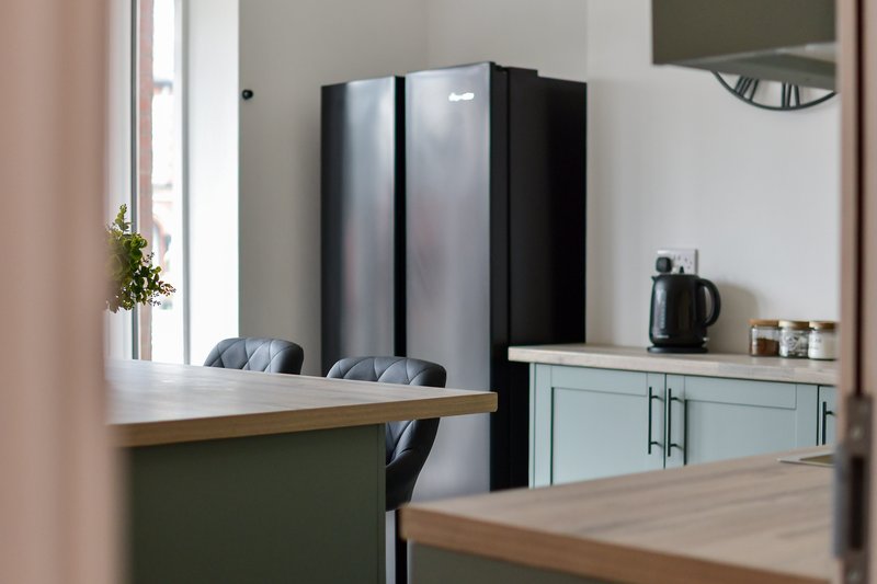 Modern kitchen with wooden countertop, black refrigerator, light green cabinetry and kettle