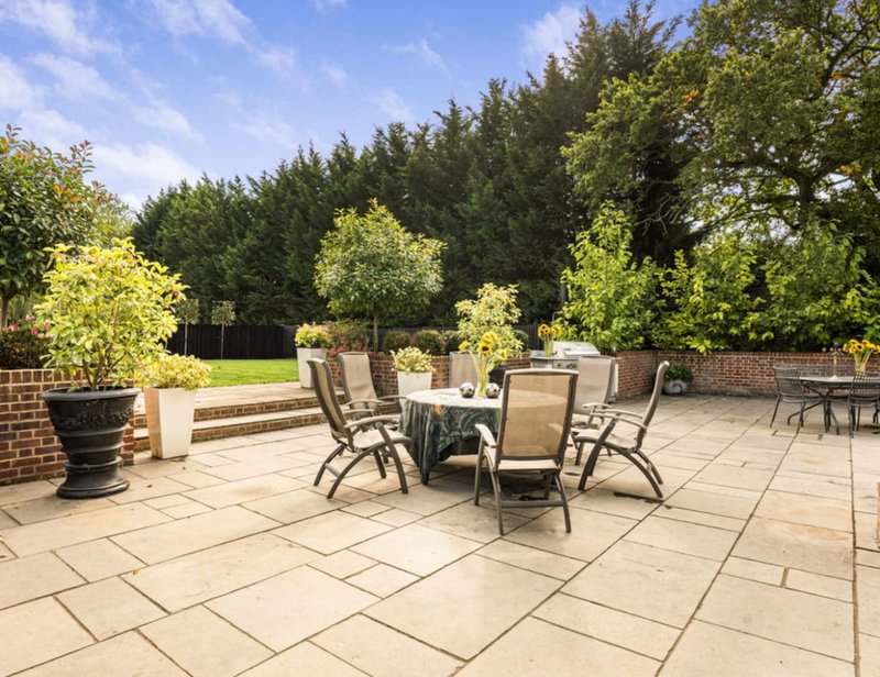 Spacious paved terrace with outdoor dining furniture and landscaped garden borders