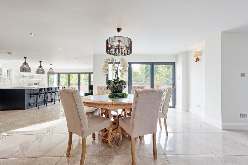 Open-plan dining and kitchen area with round wooden table, upholstered chairs, and pendant lighting