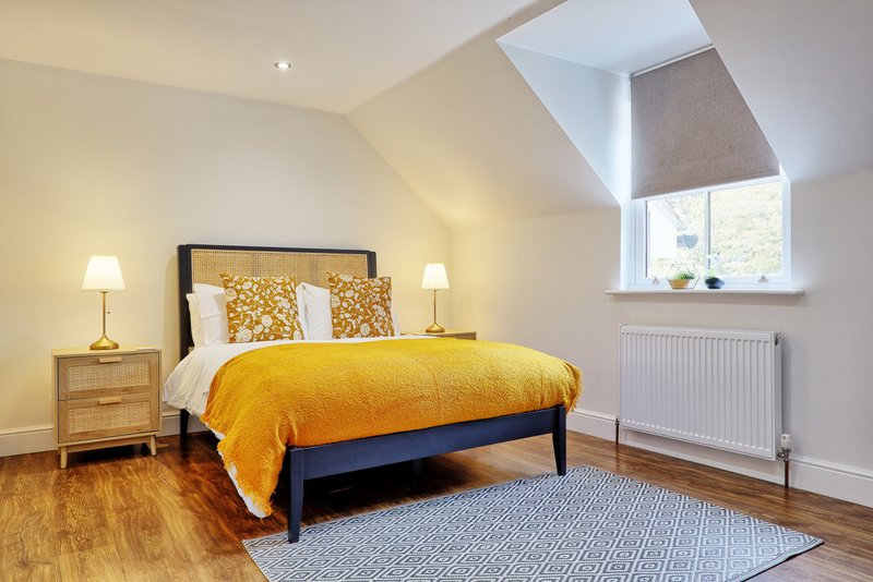 Bright bedroom with double bed, yellow bedding, wooden nightstand, skylight window and wooden floor