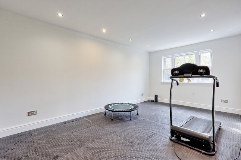 Spacious gym room with treadmill, exercise trampoline, white walls and recessed lighting