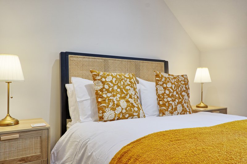 Bedroom with double bed, gold patterned pillows, white bedding, and brass lamps