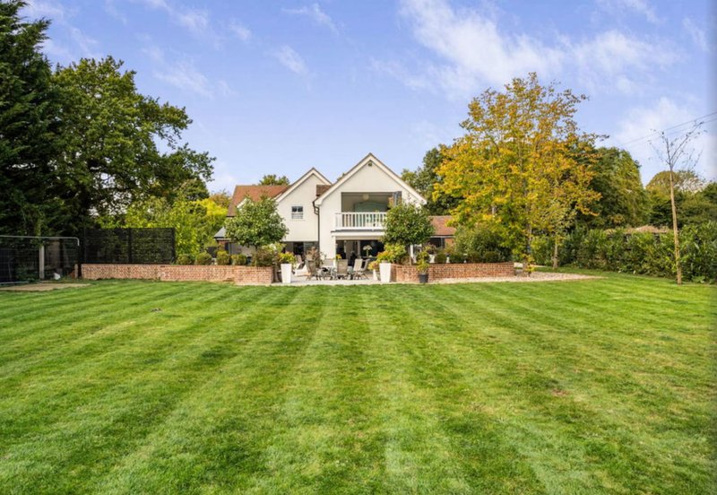 Large two-storey house with manicured lawn, surrounding trees and clear blue sky