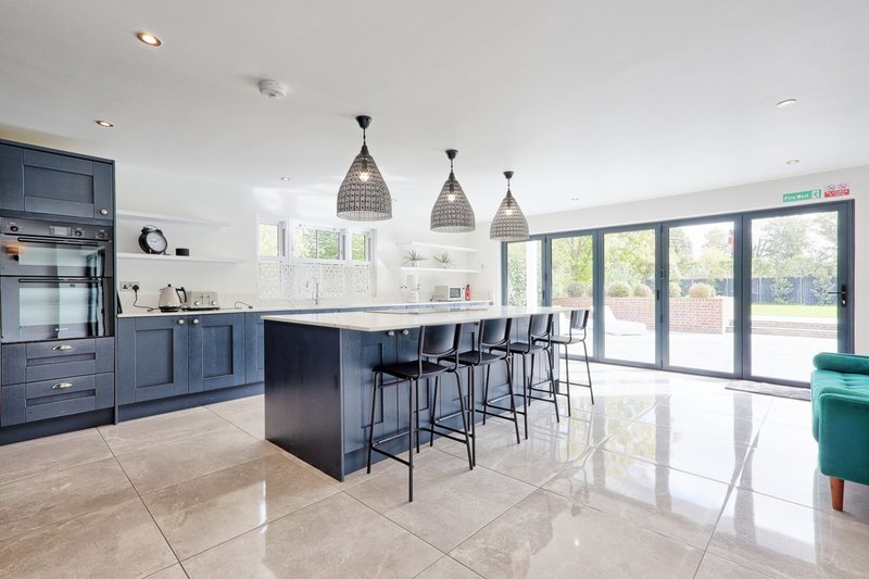 Modern open-plan kitchen with island, bar seating, pendant lights and glass doors to garden