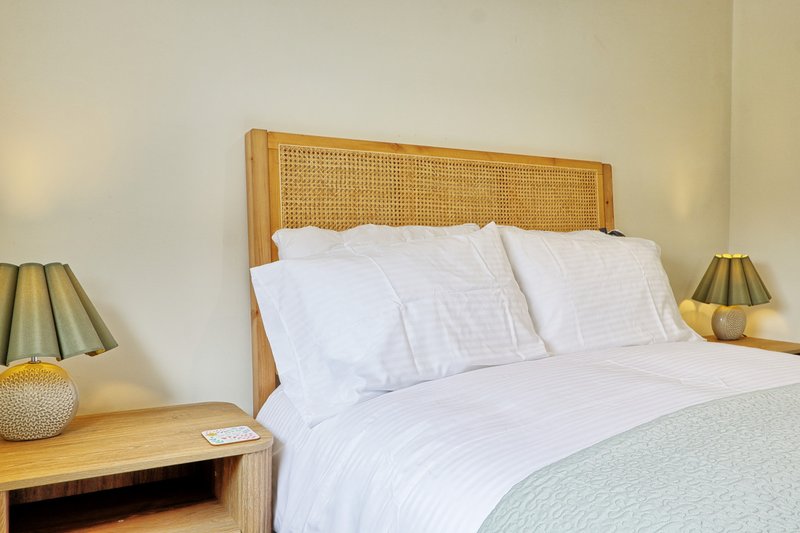 Bedroom with wooden bed frame, rattan headboard, white bedding, and matching wooden nightstands with lamps