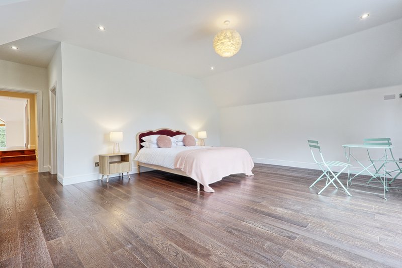 Spacious modern bedroom with wooden flooring, double bed, pendant light fixture and seating area