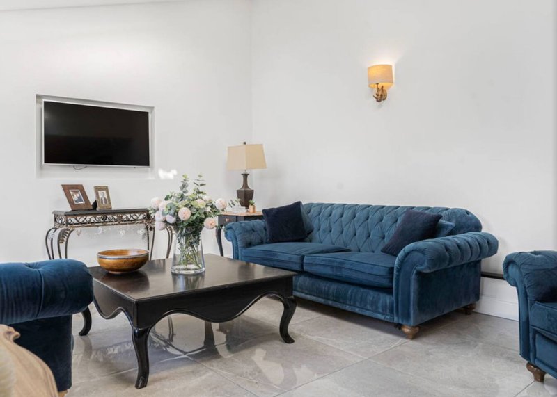 Spacious living room with blue upholstered sofa, black coffee table, wall-mounted TV and elegant lighting fixtures