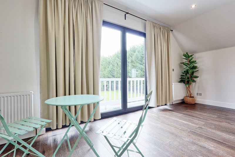 Bright attic bedroom with mint-green table, folding chairs, wooden flooring and garden views