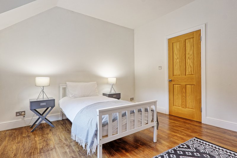 Bright bedroom with white metal bed frame, wooden floor, bedside lamps and oak door