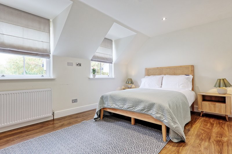 Bright attic bedroom with wooden bed, white bedding, wooden nightstands and warm wood flooring