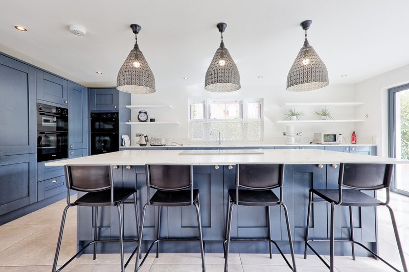 Modern kitchen with blue cabinetry, white countertop, island seating, and pendant lighting