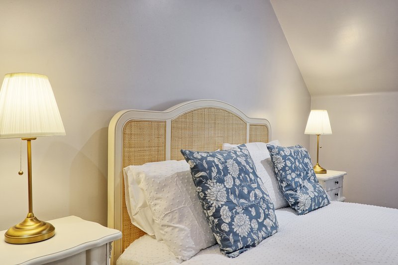 Bright bedroom with wooden headboard, white bedding, blue patterned pillows and brass table lamp