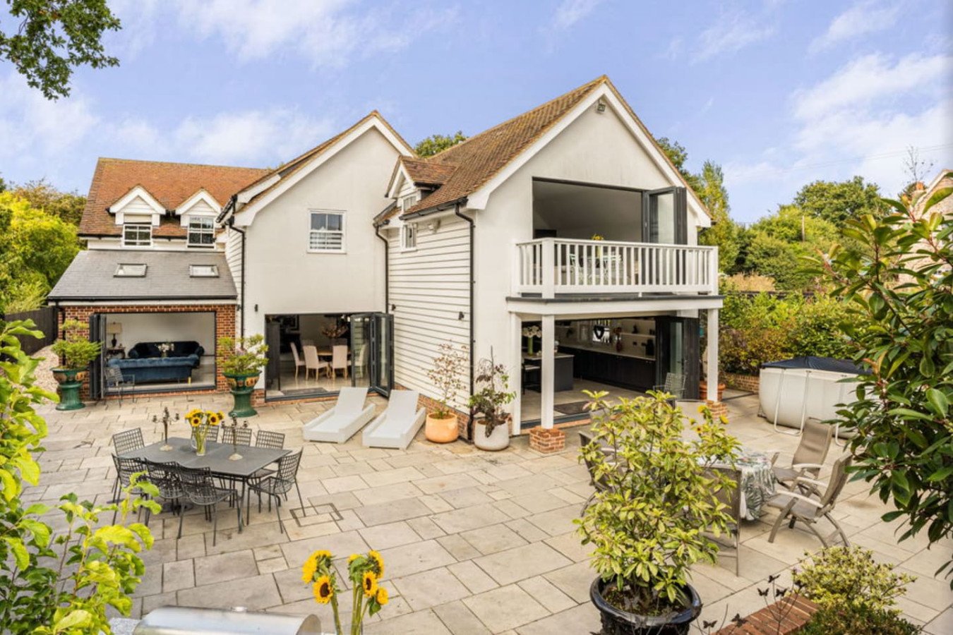 Cream-coloured house with garage, patio seating area and manicured garden surrounded by greenery
