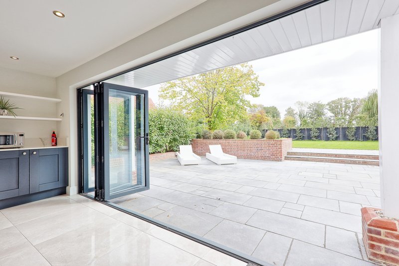 Modern kitchen with bi-fold doors opening onto large paved terrace and garden