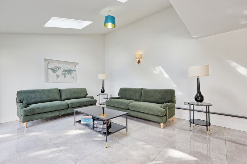 Bright modern living room with two green sofas, glass coffee table, and pendant lighting