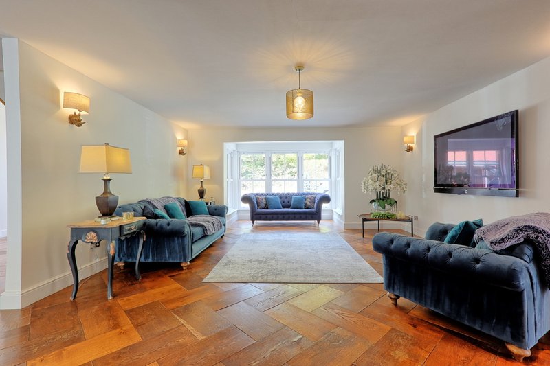 Spacious living room with two navy sofas, wooden herringbone floor, table lamps, wall-mounted TV and pendant lighting