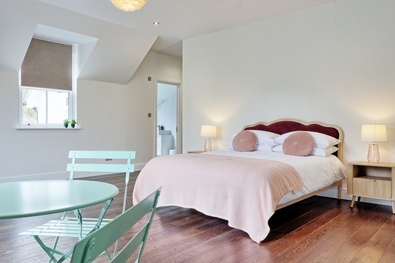 Spacious bedroom with double bed, burgundy headboard, pink cushions, wooden floor and seating area