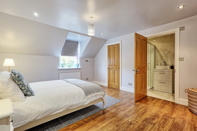 Modern attic bedroom with double bed, wooden flooring, skylight window and en-suite bathroom door