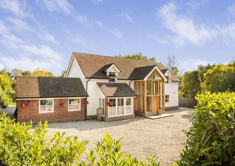 Modern brick and white house with pitched roof, driveway, and surrounding garden landscaping