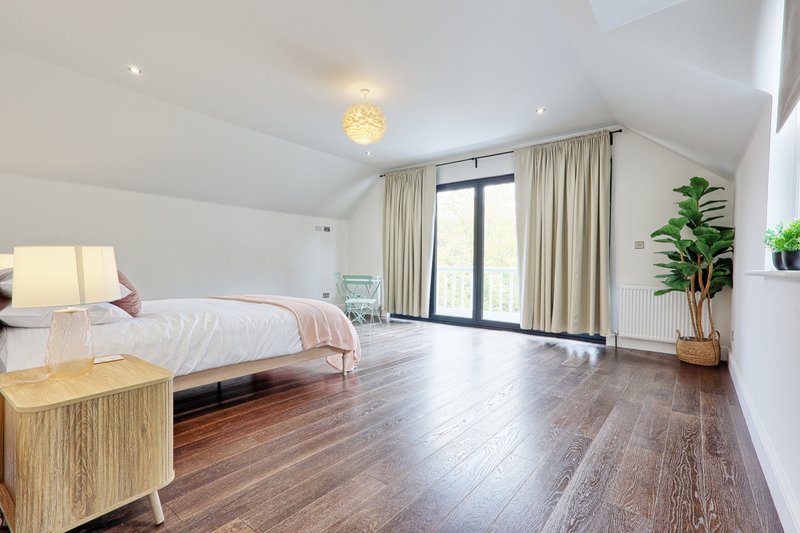 Spacious modern bedroom with wooden flooring, bed, bedside lamp and potted plant