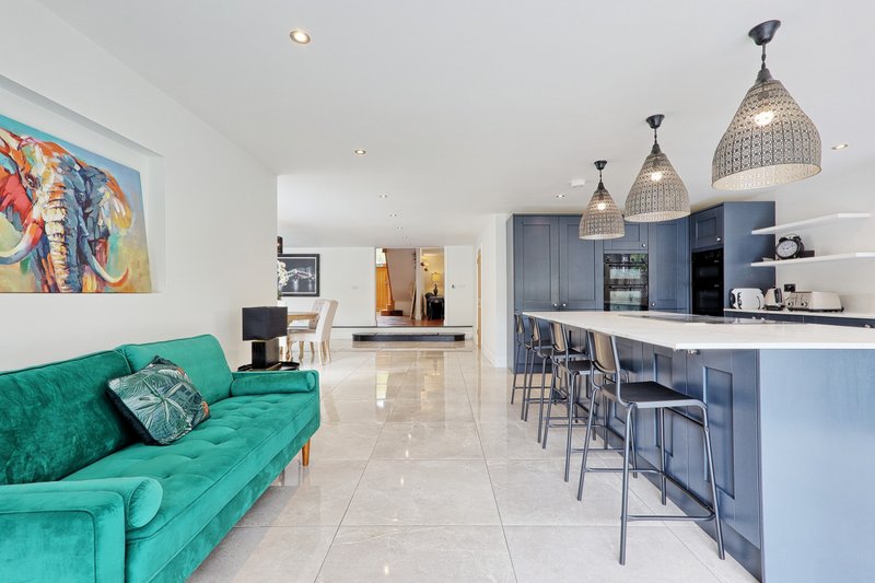 Open-plan living and kitchen area with green sofa, blue cabinetry, and pendant lights