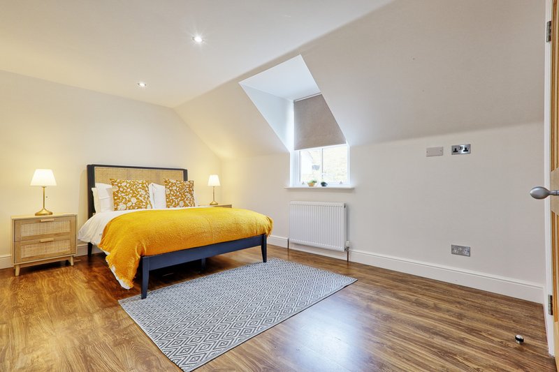 Bright attic bedroom with yellow bedding, wooden furniture, skylight and wooden flooring