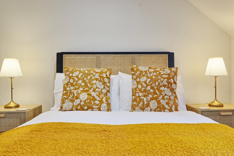 Bedroom with double bed, yellow bedspread, patterned cushions and bedside lamps