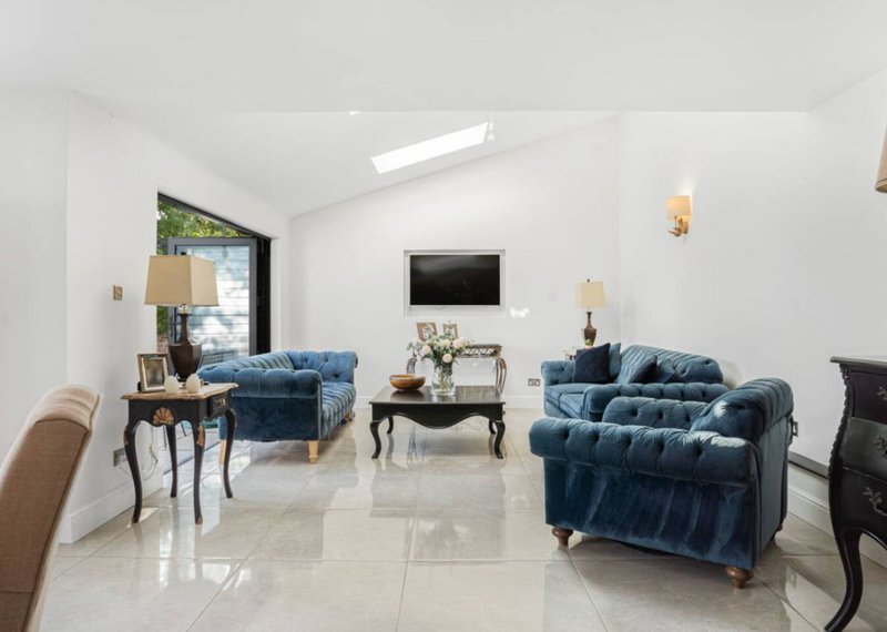 Bright open-plan living room with blue upholstered armchairs, coffee table, wall-mounted TV, and skylights