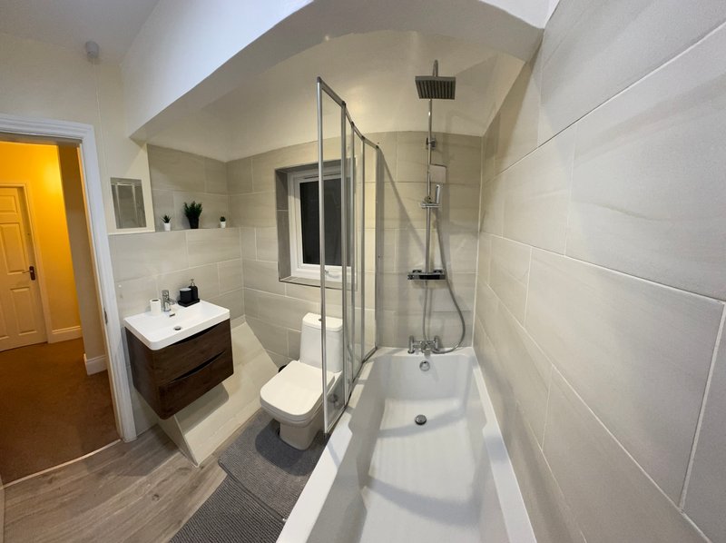 Modern bathroom with white tile walls, bathtub with shower enclosure, toilet, vanity sink and yellow door