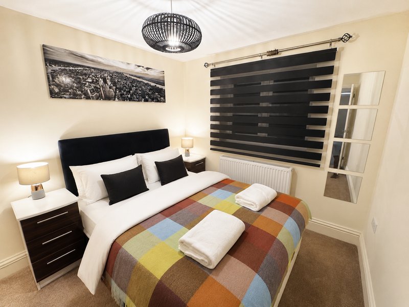 Modern bedroom with black headboard, double bed, colorful patchwork throw, and striped window blinds