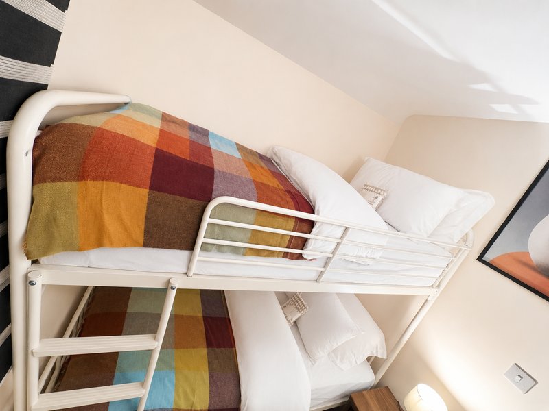 Bunk bed with colorful plaid blanket and white bedding in compact bedroom