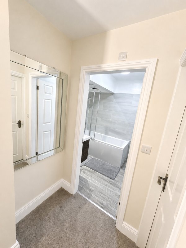 Hallway with cream walls, grey carpet, white doors and modern ensuite bathroom entrance