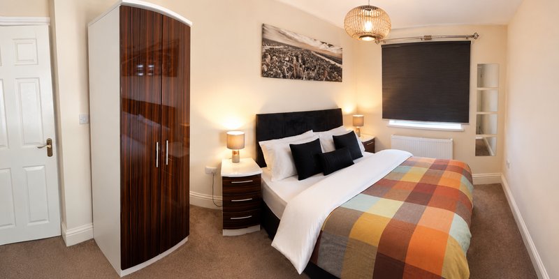 Bedroom with double bed, black headboard, plaid bedding, wooden wardrobe and pendant lighting