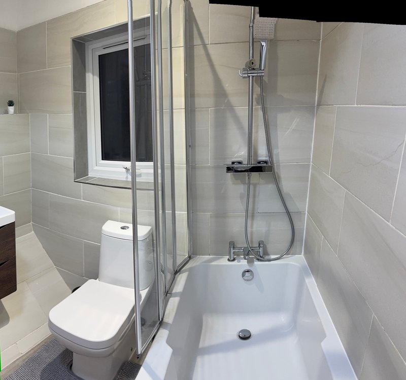 Modern bathroom with white toilet, bathtub, shower enclosure and window