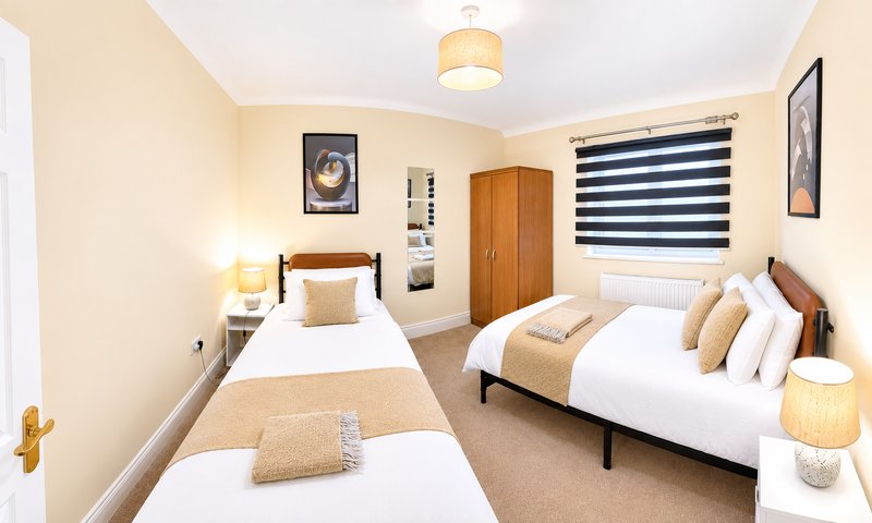 Spacious bedroom with two single beds, wooden wardrobe, and neutral décor