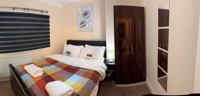 Bedroom with double bed, colorful patchwork bedding, dark wardrobe and window blinds