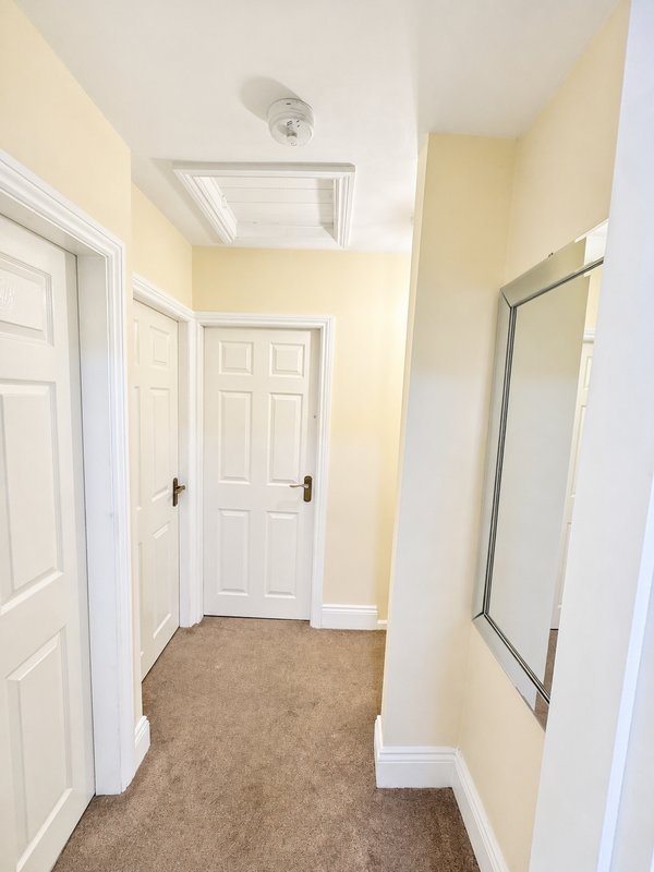 Hallway with pale yellow walls, white doors, carpeted floor and ceiling vent