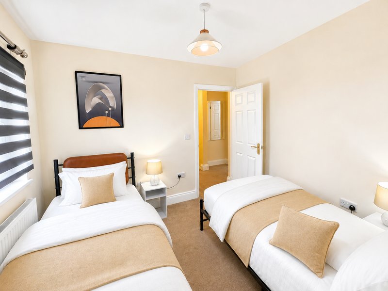 Twin bedroom with two single beds, wooden frames, beige bedding, pendant light and framed wall art