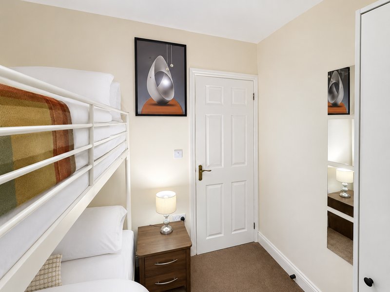 Bedroom with white bunk bed, wooden nightstand, abstract wall art, and white door