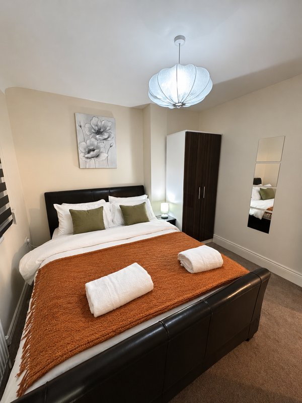 Modern bedroom with double bed, orange throw, white pillows and pendant light fixture